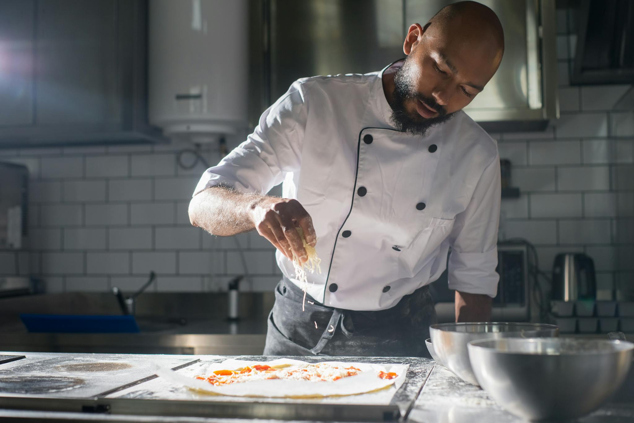 A professional chef adds cheese to a pizza in a modern kitchen setting.